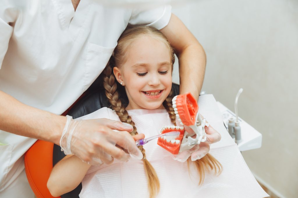 male dentist medical uniform shows little girl how properly brush her teeth jaw model dentistry concept